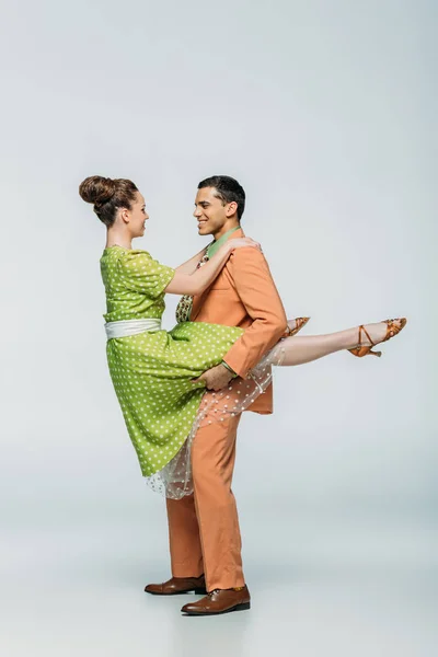 Guapo bailarín holding chica mientras bailando boogie-woogie en gris fondo - foto de stock