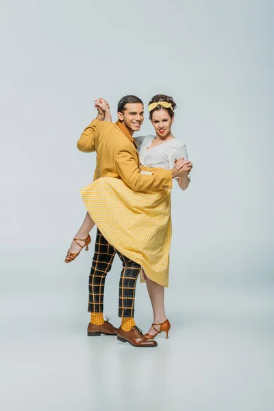 Smiling dancers holding hands while dancing boogie-woogie on grey background — Stock Photo