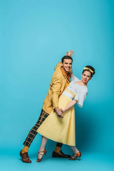 Stylish dancers holding hands while dancing boogie-woogie on blue background — Stock Photo