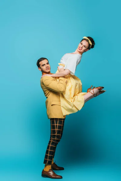 Bonito dançarino segurando menina enquanto dança boogie-woogie no fundo azul — Fotografia de Stock