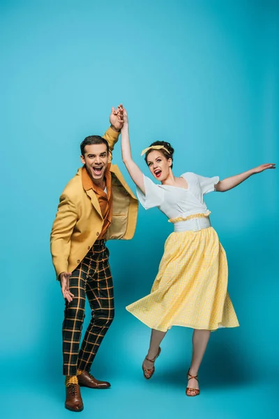 Bailarines felices tomados de la mano mientras bailan boogie-woogie sobre fondo azul - foto de stock