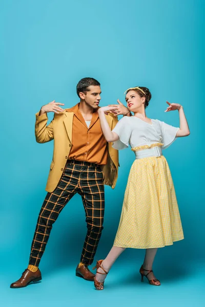 Bailarines elegantes mirándose mientras bailan boogie-woogie sobre fondo azul - foto de stock