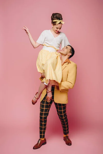 Guapo hombre sosteniendo feliz chica mientras bailando boogie-woogie sobre rosa fondo - foto de stock