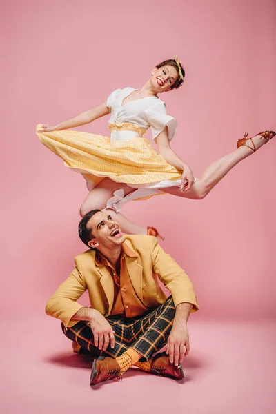 Cheerful man sitting on floor and happy girl jumping while dancing boogie-woogie on pink background — Stock Photo