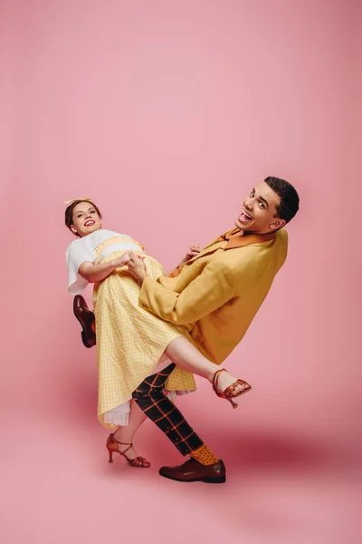 Alegre pareja mirando cámara mientras bailando boogie-woogie sobre rosa fondo - foto de stock