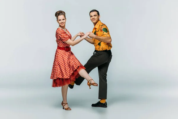 Danseurs élégants regardant la caméra tout en dansant boogie-woogie sur fond gris — Photo de stock