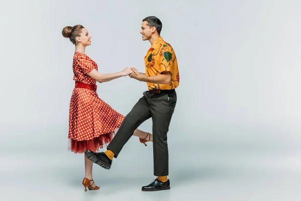 Seitenansicht eines lächelnden Paares, das Händchen hält, während es Boogie-Woogie auf grauem Hintergrund tanzt — Stockfoto