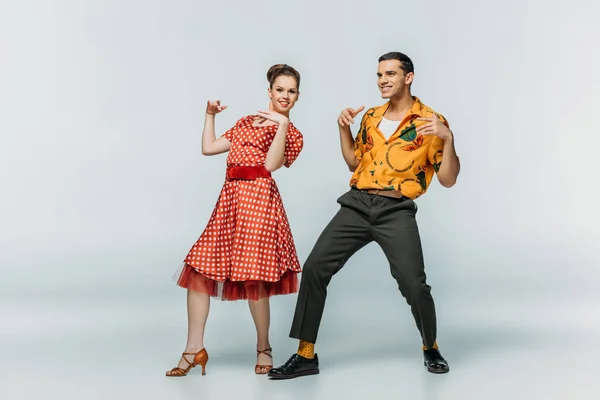 Sorrindo casal olhando para a câmera enquanto dança boogie-woogie no fundo cinza — Fotografia de Stock