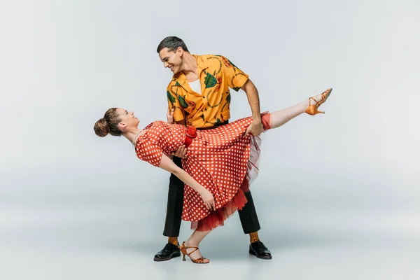 Smiling man holding woman while dancing boogie-woogie on grey background — Stock Photo