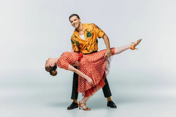 Cheerful man supporting woman while dancing boogie-woogie on grey background — Stock Photo