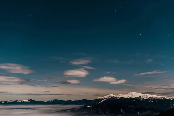 Vista panorâmica de montanhas nevadas com nuvens brancas fofas à noite — Fotografia de Stock