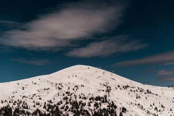 Живописный вид горы, покрытой снегом и соснами против темного неба вечером — стоковое фото