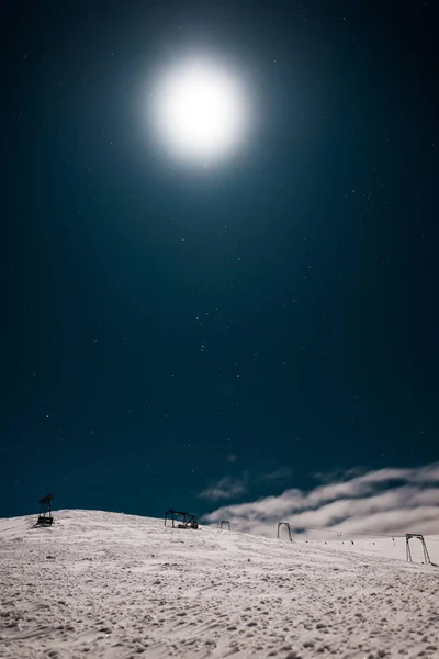 Scenic view of gondola lift in mountain covered with snow against dark sky with shining sun — Stock Photo