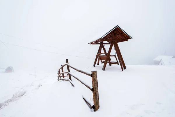 Cerca de madera y columpio en el pueblo de montaña nevado en la niebla - foto de stock