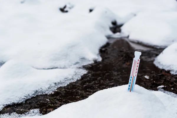 Termómetro en la nieve cerca de la corriente de la montaña - foto de stock