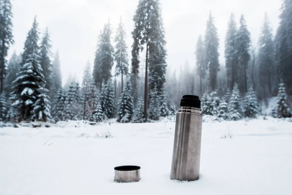 Vacuum flask on snow in mountains with pine trees — Stock Photo