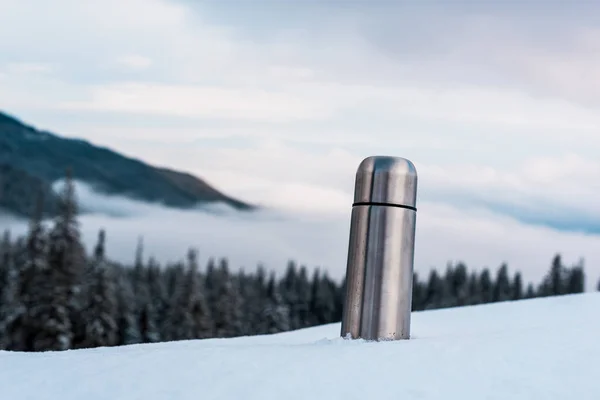 Frasco de vacío metálico en montañas nevadas con pinos y nubes blancas esponjosas - foto de stock