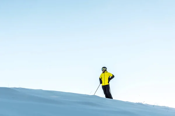 Skifahrer im Helm hält Stöcke im Stehen mit der Hand an der Hüfte — Stockfoto