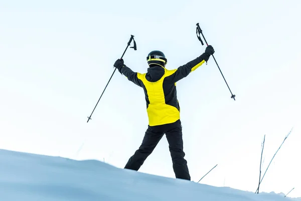 Back view of skier in helmet holding sticks while standing on white snow — Stock Photo