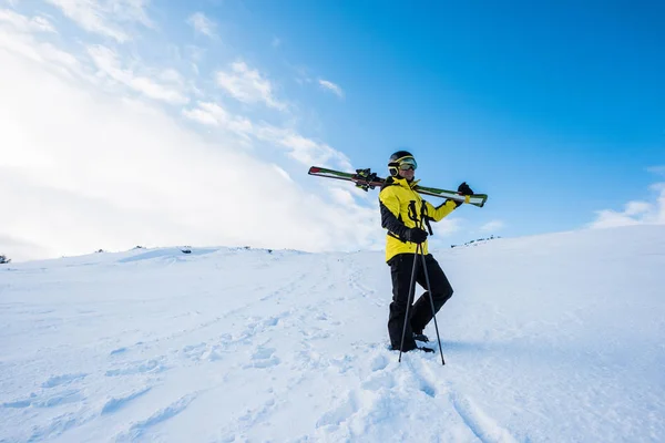 Sportsman in helmet standing with ski sticks on snow in mountains — Stock Photo