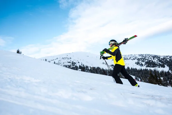 Vue latérale du skieur marchant avec bâtons de ski sur la neige — Photo de stock