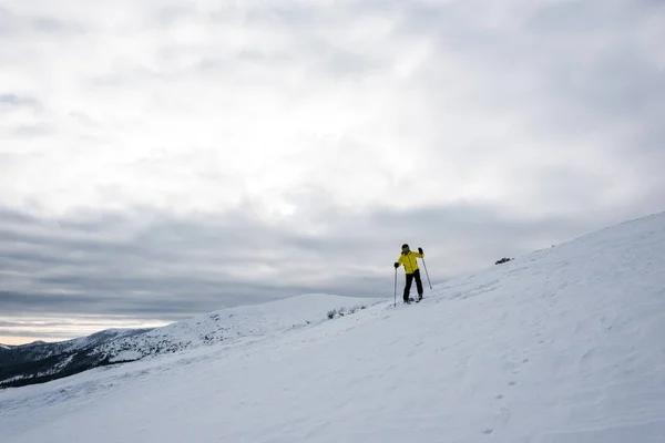 Skier in helmet standing with ski sticks on slope in cold wintertime — Stock Photo