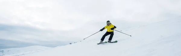 Panoramic shot of sportsman holding ski sticks while skiing on white snow — Stock Photo