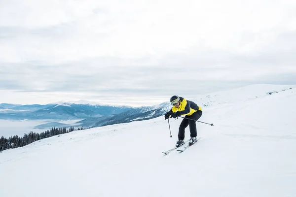 Sportsman holding ski sticks and skiing on white slope in mountains — Stock Photo