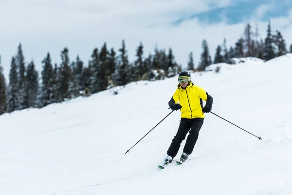 Лыжник в шлеме держит палки и катается на лыжах по склону в горах — стоковое фото