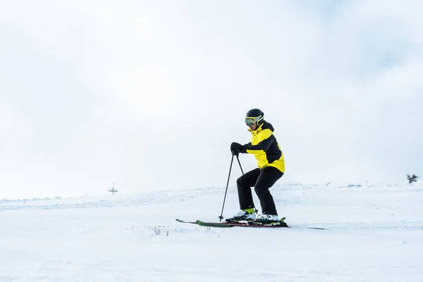 Sportsman in helmet holding sticks and skiing on slope with snow — Stock Photo