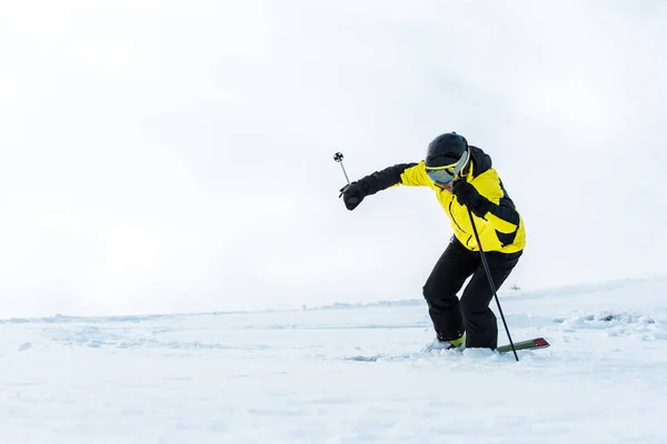 Deportista con gafas sosteniendo palos y esquiando en pista con nieve - foto de stock