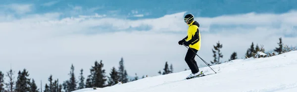 Panoramic shot of sportsman in helmet skiing on slope near mountains — Stock Photo