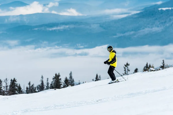 Skieur en casque tenant des bâtons et skiant sur la piste en hiver — Photo de stock
