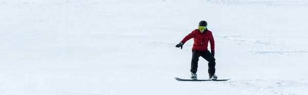 Tiro panorâmico de snowboarder no capacete montando na encosta com neve branca fora — Fotografia de Stock