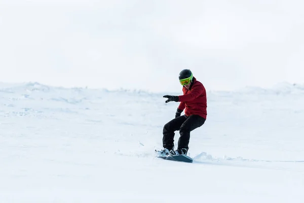 Snowboarder atlético en casco a caballo en la pendiente exterior - foto de stock