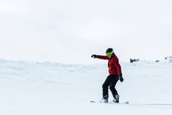 Snowboarder atlético en casco y gafas de montar en la pendiente exterior - foto de stock