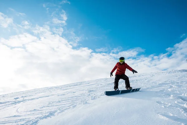 Snowboarder atlético en casco montado en la pendiente contra el cielo azul con nubes - foto de stock