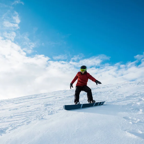 Snowboarder in casco cavalcando sul pendio contro il cielo blu — Foto stock