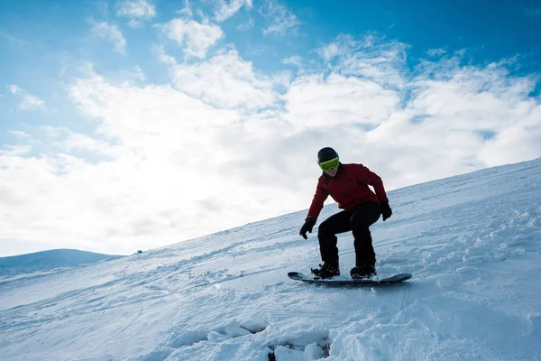 Snowboarder atlético montando na inclinação contra o céu azul no inverno — Fotografia de Stock