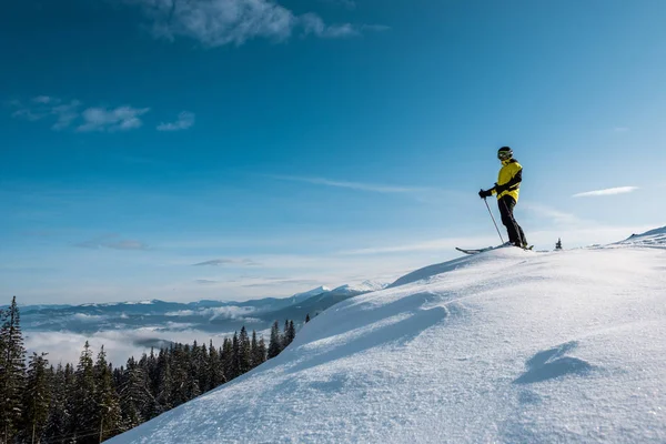 Лыжник держа лыжные палочки и стоя против голубого неба в горах — стоковое фото
