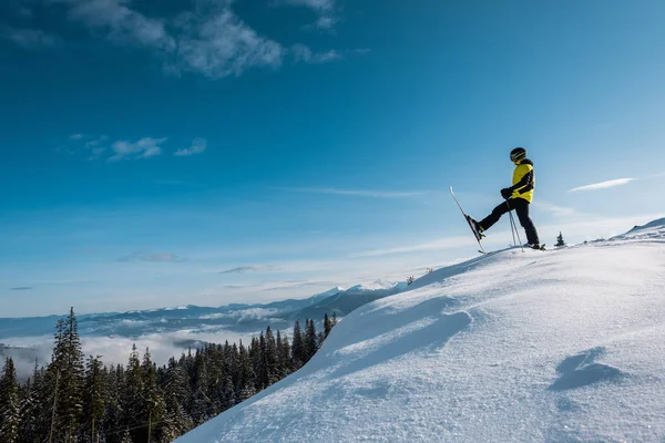 Vue latérale du skieur tenant des bâtons de ski et faisant un pas contre le ciel bleu en montagne — Photo de stock