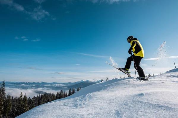 Vista lateral del esquiador sosteniendo bastones de esquí y dando paso contra el cielo en las montañas - foto de stock