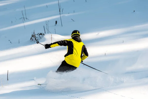 Back view of sportsman in helmet holding ski sticks while skiing on snow — Stock Photo