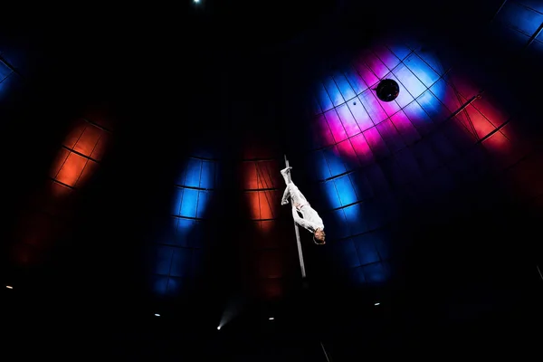 Low angle view of acrobat performing upside down on pole in arena of circus — Stock Photo