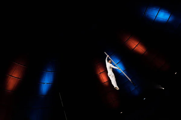 Low angle view of athletic acrobat balancing on metallic pole in arena of circus — Stock Photo