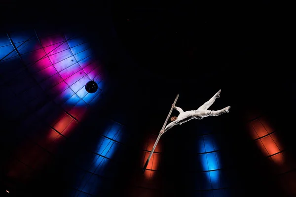 Vue à faible angle de l'acrobate athlétique équilibrage sur pôle métallique près de l'éclairage bleu et rouge dans l'arène — Photo de stock