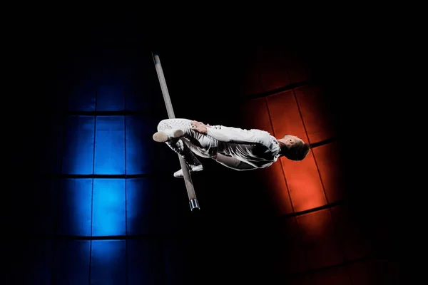 Athletic acrobat balancing on metallic pole near blue and red lighting in circus — Stock Photo