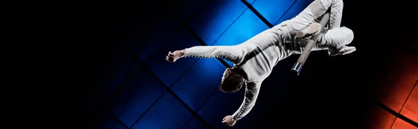 Plano panorámico de acróbata balanceándose en poste metálico cerca de la iluminación azul y roja en circo - foto de stock