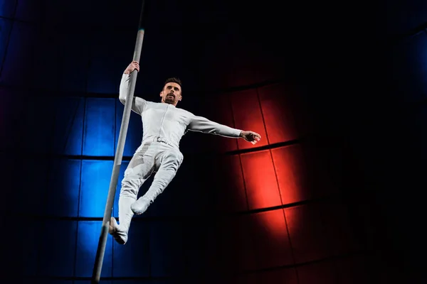 Strong acrobat holding metallic pole while performing in circus — Stock Photo