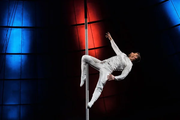 Side view of strong acrobat holding metallic pole with leg while performing in circus — Stock Photo